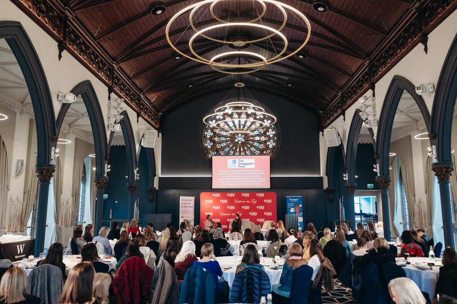 A full hall of seated attendees under chandeliers