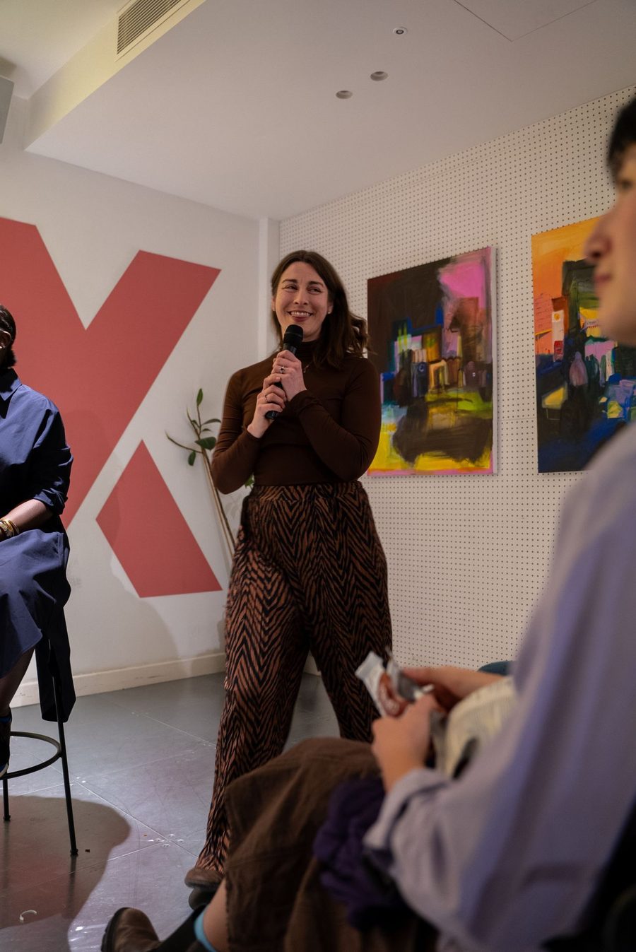 Milly speaking with a microphone in front of a large red X