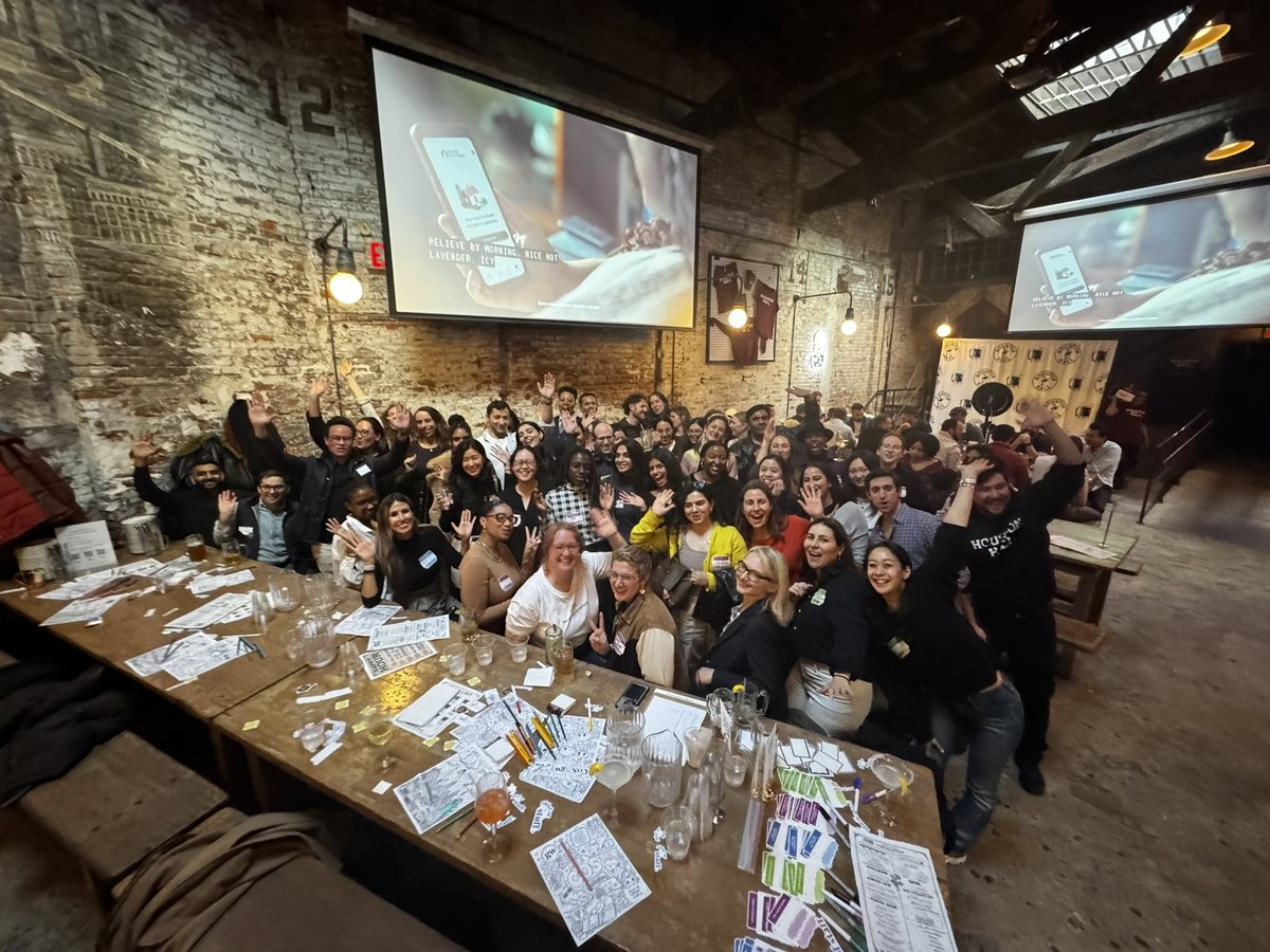 A large workshop crowd in a brick venue with hands in the air